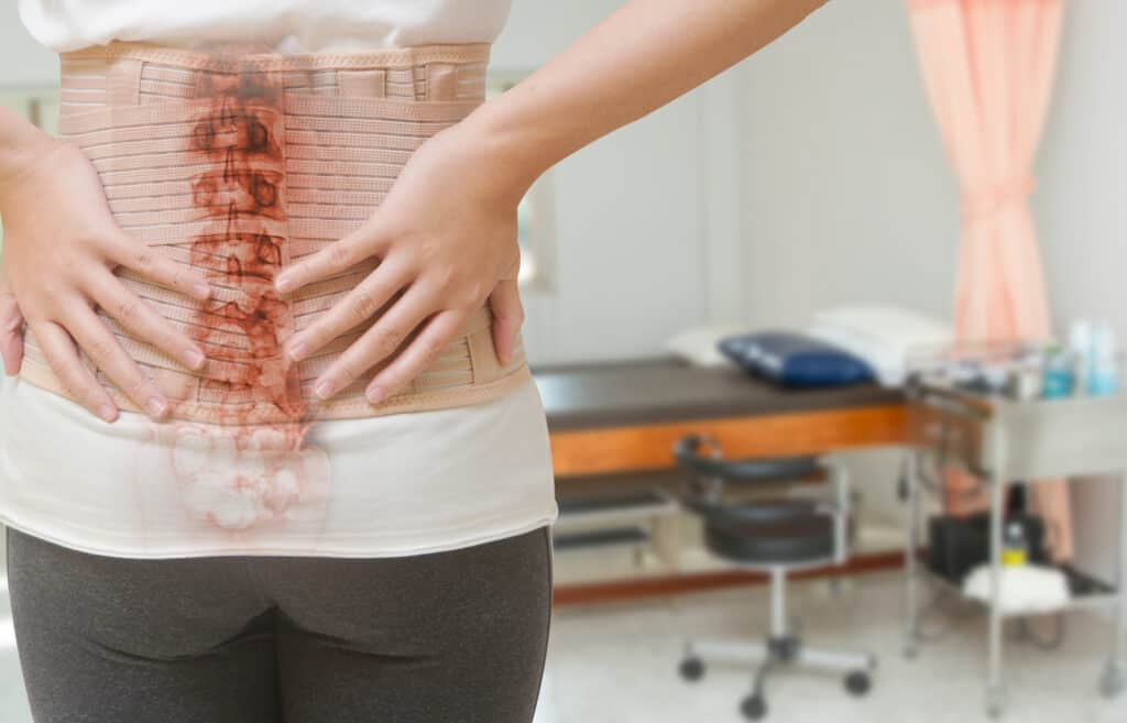 Woman in back pain from spinal injury wearing lumbar brace corset at hospital