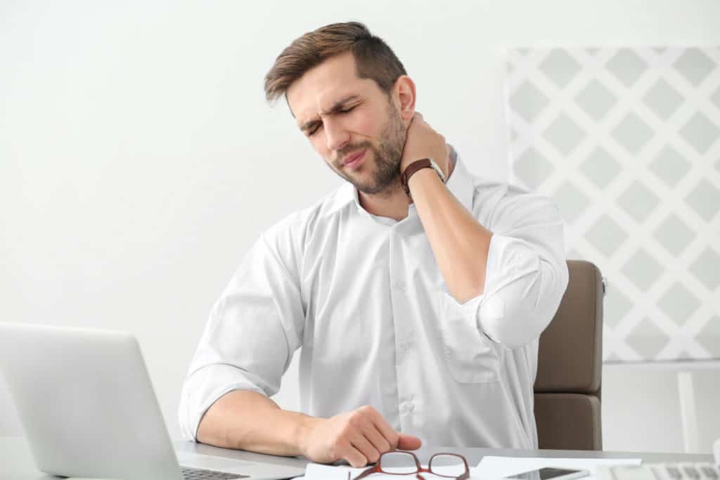 man sitting at desk holding his neck in pain