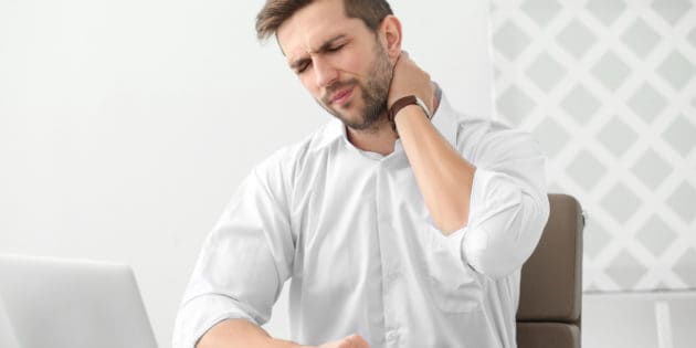 man sitting at desk holding his neck in pain