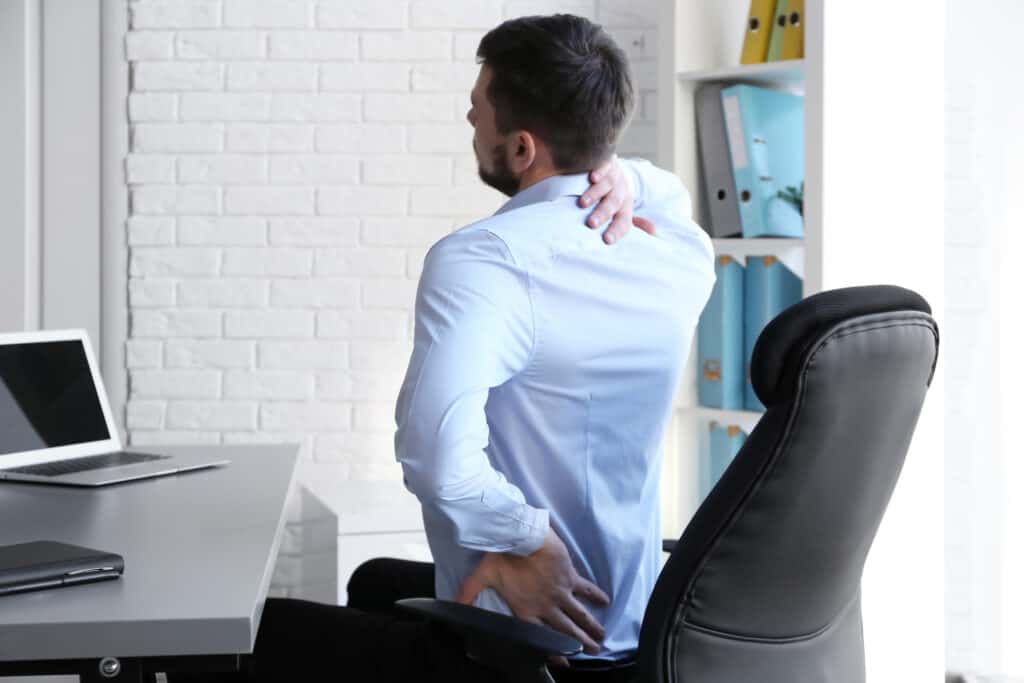 Posture concept. Man suffering from back pain while working with laptop at office poor posture