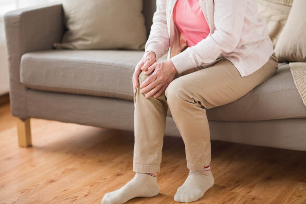 Elderly women holding her knee in pain whilst sitting down 