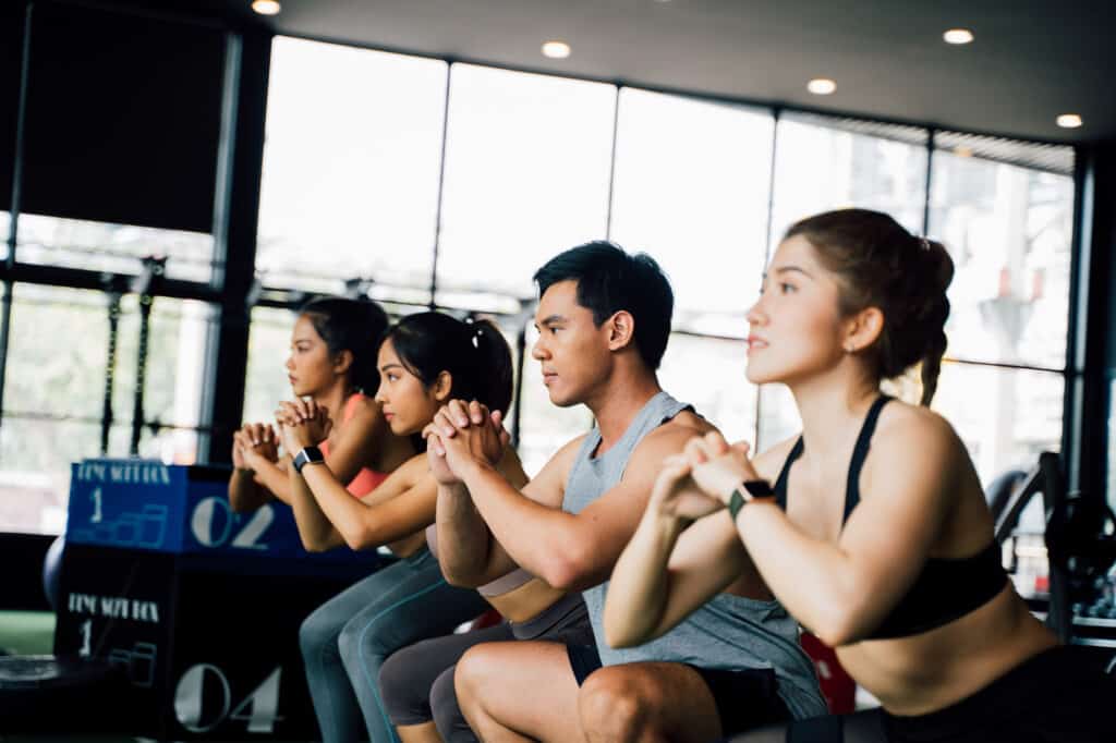 High-intensity workouts Group of athletic young Asian people in sportswear doing squat and exercising at the gym. Intense workout and healthy lifestyle concept