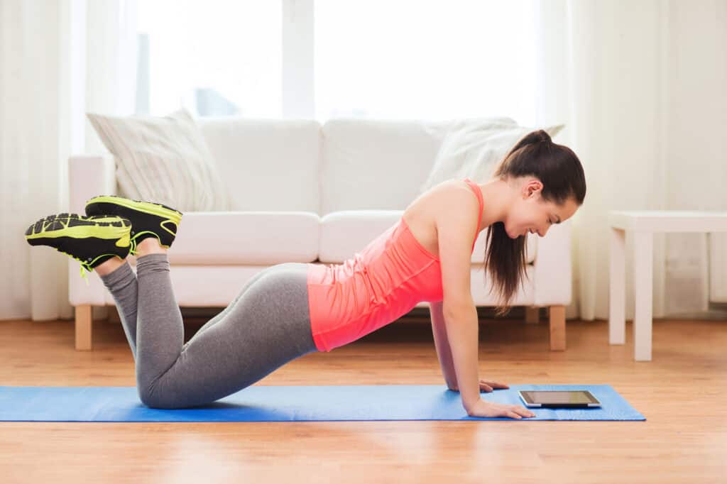 fitness, home, technology and diet concept - smiling teenage girl doing push-ups and looking at tablet pc computer at home