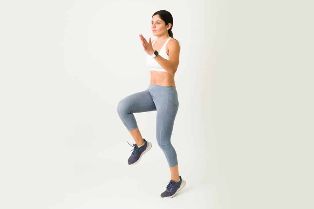Beautiful caucasian woman jumping and running in place for a high intensity interval training. Female athlete with a strong core doing cardio and HIIT High-Intensity Interval Training