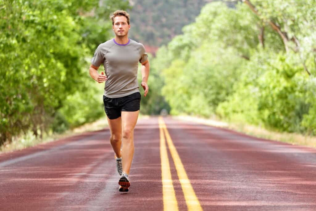 HIIT Sport and fitness runner man running on road training for marathon run doing high intensity interval training sprint workout outdoors in summer. Male athlete sports model fit and healthy aspirations.