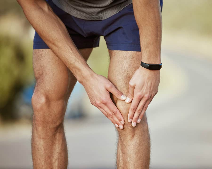 Closeup shot of a man holding his knee in pain while exercising outdoors