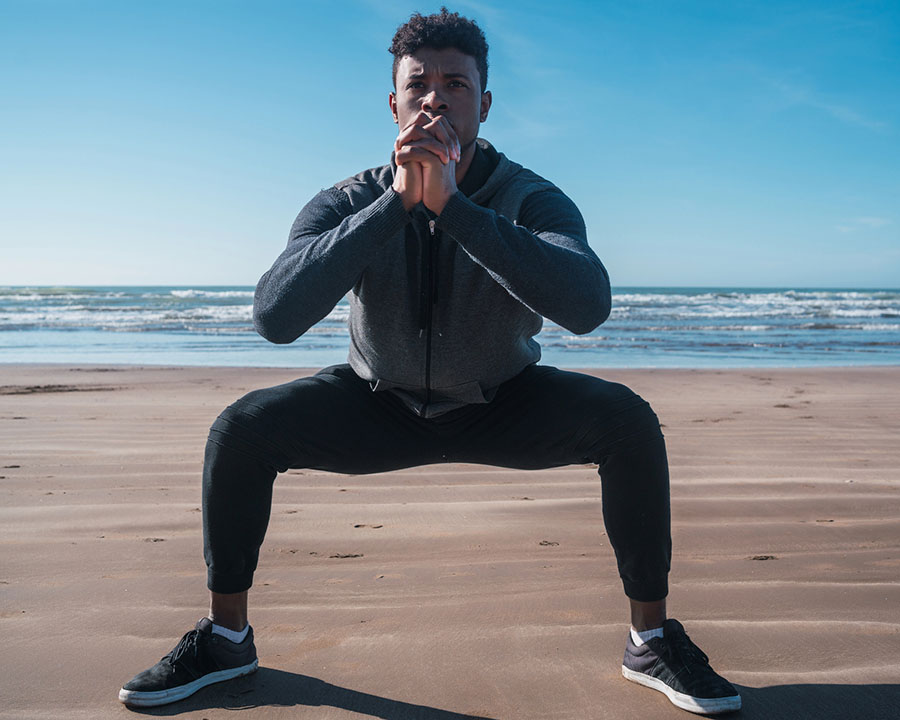 man doing a squat on the beach