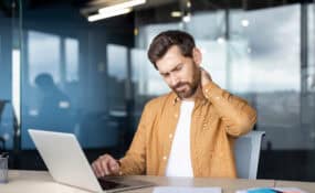 Man at work experiencing neck discomfort while seated at a desk
