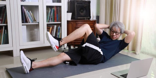 a man doing sit ups on a mat in front of a laptop