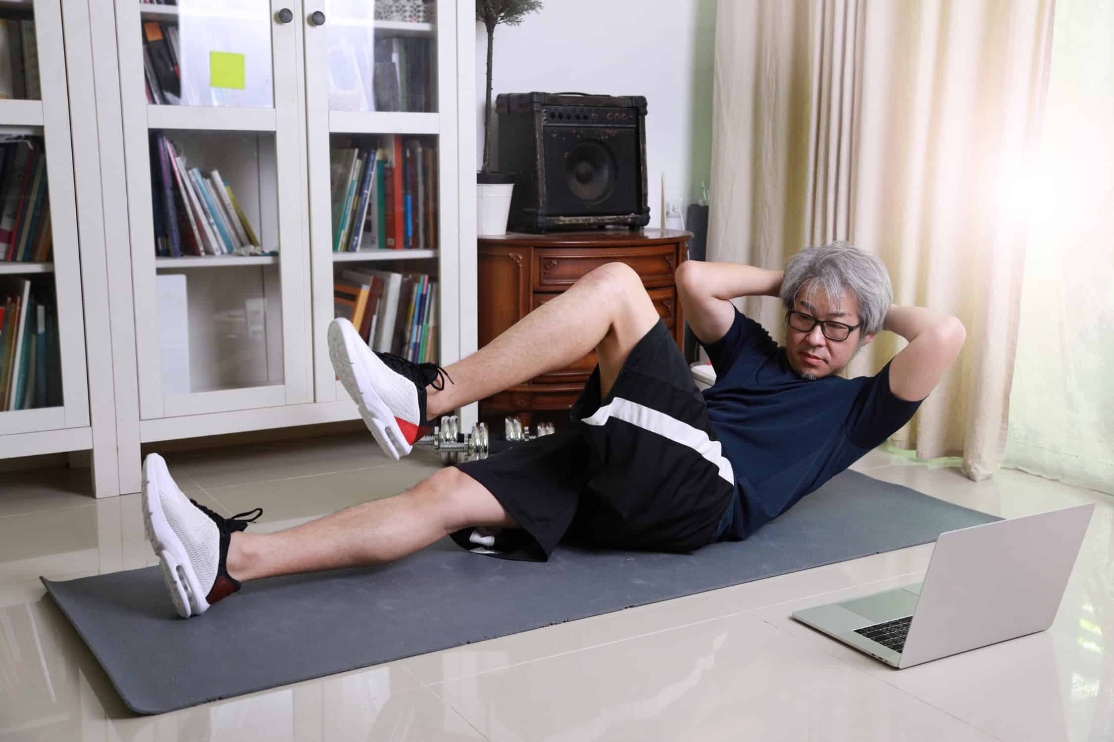 a man doing sit ups on a mat in front of a laptop