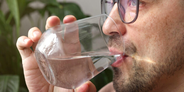 a man drinking from a glass wondering how much water should I drink a day?