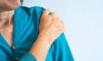 a close up of a hand on a woman's shoulder doing frozen shoulder exercises