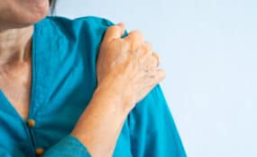 a close up of a hand on a woman's shoulder doing frozen shoulder exercises