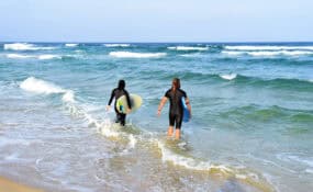 two people walking in the water with surfboards surfing