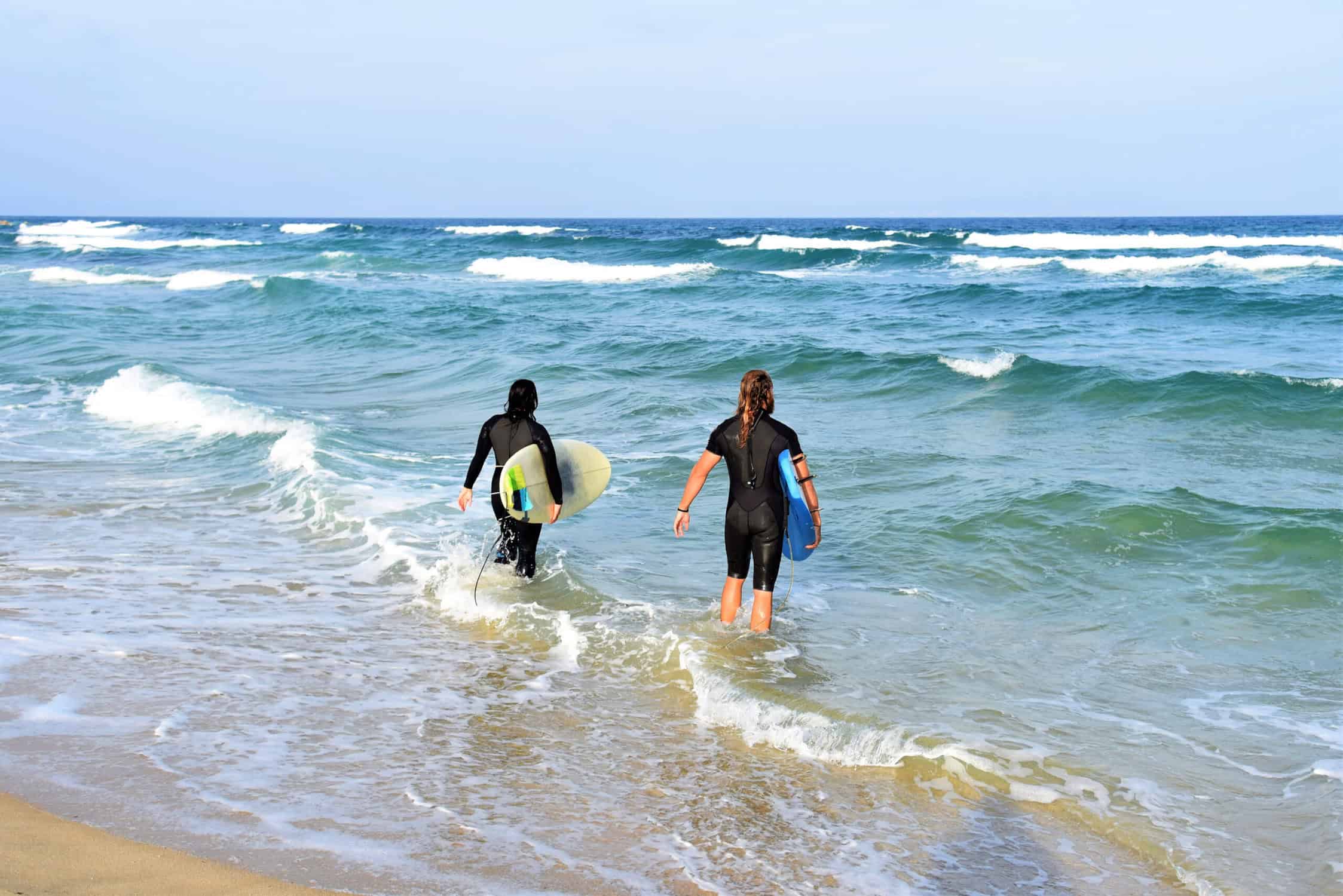 two people walking in the water with surfboards surfing